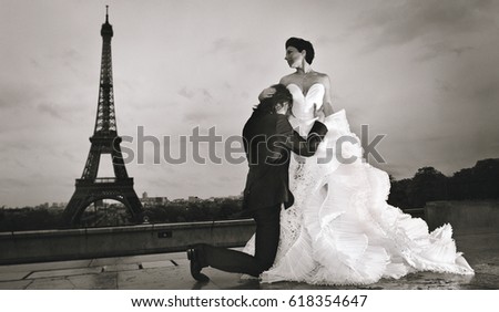 An attractive young married couple, in elegant and traditional wedding clothes, dancing and posing in a scenic location in Paris with the Eiffel Tour on the background