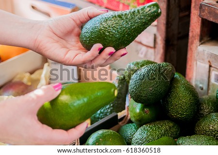 Cropped image of a customer choosing avocados in the supermarket. close up of woman hand holding avocado in market. sale, shopping, food, consumerism and people concept 
