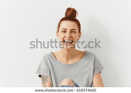 People, youth, leisure and lifestyle concept. Fashionable tattooed young Caucasian young female student wearing stylish clothing laughing happily, having rest at home after lectures at college