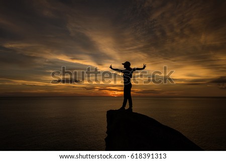 silhouette of woman hand up and standing on rock in sunset.