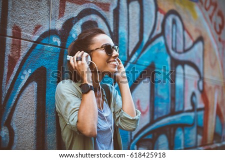 Young woman listening to music via headphones on the street Royalty-Free Stock Photo #618425918