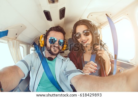 Happy smiling couple making selfie with smartphone inside plane cabin during flight. Young man and woman enjoying trip