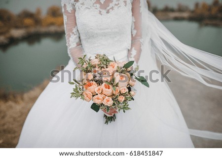 Wedding bouquet of pink roses in bride's hands on a background of lake.
