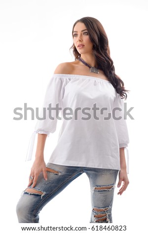 Fashionable looking girl wearing Ripped Jeans and white mini dress with silver jewellery posing at studio location on white background