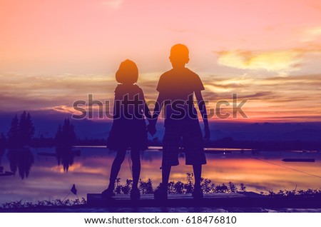Brother and sister holding hands together with sun set.