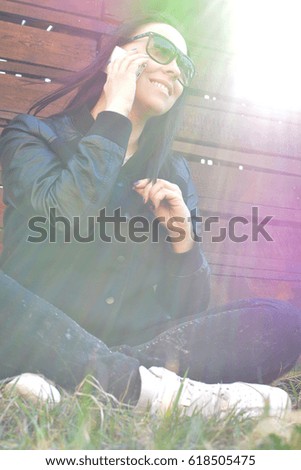 Teen girl sitting on green lawn and smiling talking on the phone. Teenager. Hipster. Communication. On open air. Close-up.