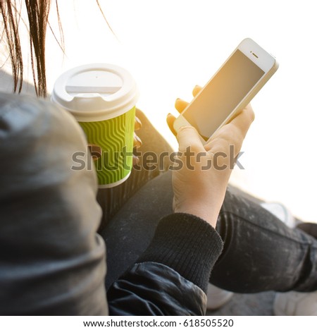 Teen girl sitting with mobile phone and coffee in hands, on concrete ancient stone floors. Teenager. Hipster. Communication. On open air. Close-up.