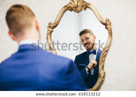 A handsome man in a suit looks in the mirror Royalty-Free Stock Photo #618513212