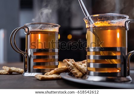 Two glasses of hot yellow tea in glass glasses with metal coasters in the studio.