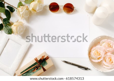 White desk with sunglasses, roses, candles, pen and vintage white tray. Empty sheet in the middle. Celebration card concept. Top view, flat lay, copyspace.