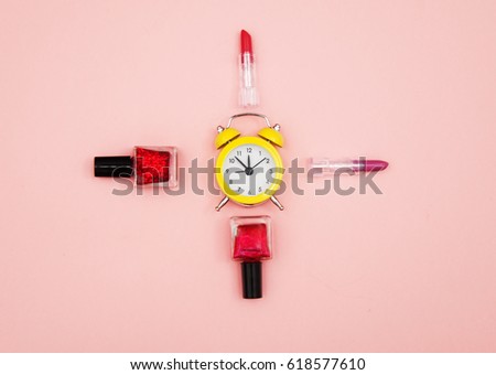 photo of lipsticks, alarm clock and nail polishes on the wonderful pink studio background