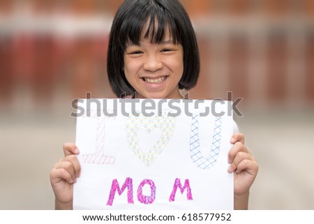 Portrait of adorable happy healthy Asia kid girl smiling holding art craft DIY card for mother with text "I love you mom" at home. Image of Asian female child for Mother's day wallpaper background.