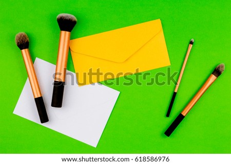 Make up brushes with yellow envelope and white blank card on greenery background. Top view. Flat lay.