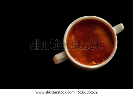 Red borscht in a white bowl isolated on a black background. Traditional Ukrainian beetroot soup with vegetables on a black table, on a black background.