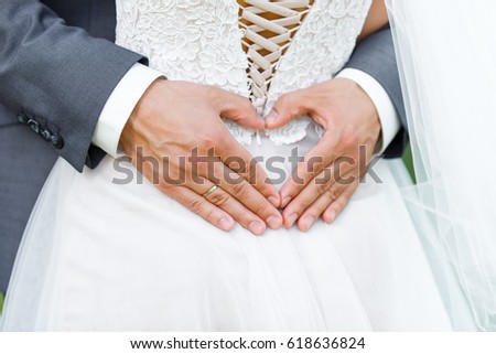 Just married groom embrace his bride and makes the shape of the heart from his hands with wedding ring. Happy and love couple