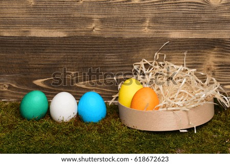 easter colorful eggs painted in bright colors with straw nest in wooden box on wood background with green moss, spring holiday celebration, copy space