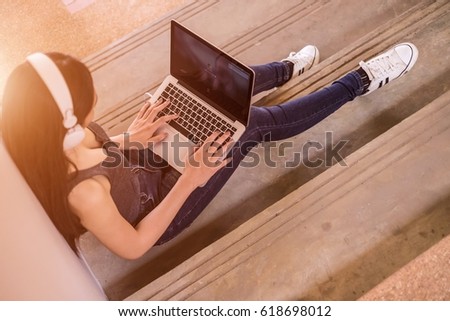 Topview young beautiful woman sitting on the staircase using laptop for search information,headphones listening music,smiling