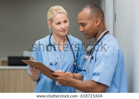 Medical multiethnic staff having discussion in a hospital hallway. Male and female nurse wearing blue scrubs working in a medical clinic. Two hospital workers discussing on laboratory test.