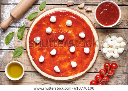 Pizza cooking preparation. Baking ingredients on the wooden table: dough, mozzarella, tomatoes sauce, basil, olive oil, tomatoes, cheese, spices. Italian food cuisine background pizza margherita
