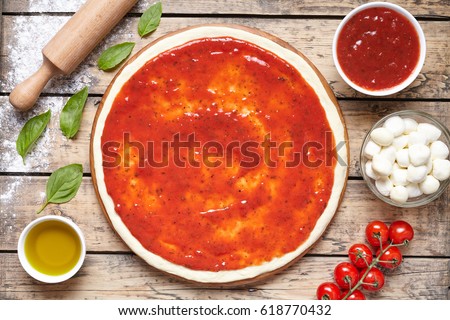 Raw dough for pizza preparation with ingredient: tomato sauce, mozzarella, tomatoes, basil, olive oil, cheese, spices served on rustic wooden table. Flat lay style. Italian pizza margheritafood