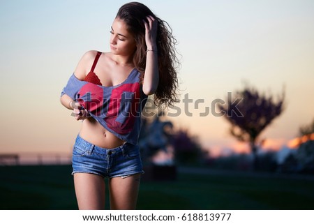 Beautiful brunette young woman with shorts and top posing above sunset background