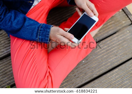 Hands holding mobile phone, wooden floor background. Person barefoot feeling relax, closeup image