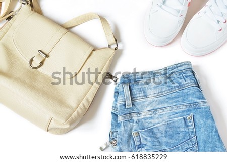 Stock photo with a collection of women's clothes. Beige bag, blue jeans in the style of 90s and trendy white sneakers. Sports chic outfit. Photography for fashion blogs