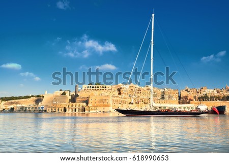 Sailing ship enters Grand Valetta bay with a view over Valetta's traditional architecture on a bright day. This picture is toned.