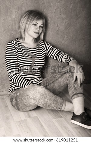 Happy woman in a striped t-shirt and jeans sitting on wooden floor