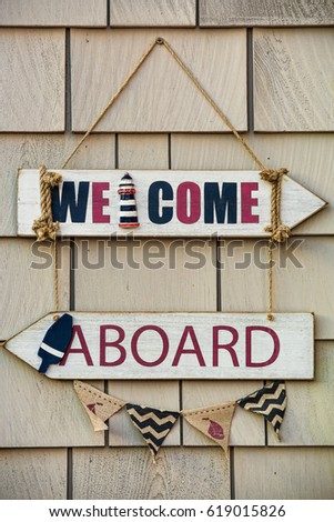 Hand painted wooden welcome aboard sign hanging on a rustic shingled building
