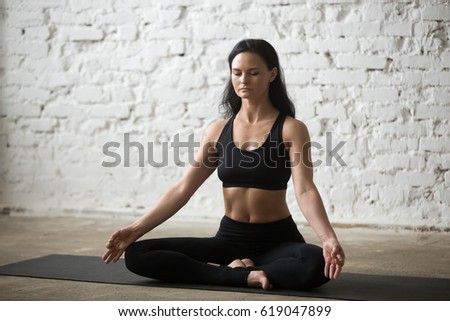 Middle aged yogi attractive woman practicing yoga concept, sitting in Half Lotus exercise, Siddhasana pose, working out, wearing black sportswear bra and pants, full length, white loft background  Royalty-Free Stock Photo #619047899