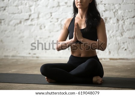 Middle aged yogi attractive woman practicing yoga concept, sitting in Sukhasana exercise, Easy Seat pose, working out wearing black sportswear bra and pants, white loft background. Midsection close up Royalty-Free Stock Photo #619048079