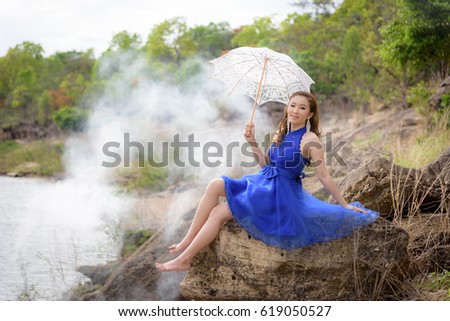 Beautiful woman wear blue evening dress hold white umbrella on the rocks.