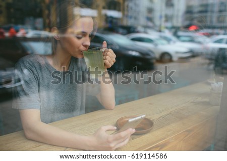 The blonde uses the phone. Girl and smartphone. A woman is sitting in a cafe with a cellular.