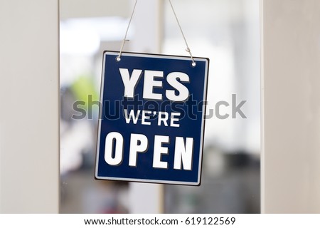 " YES we're OPEN " sign in blue and white, on shop glass door, with white painted frame.