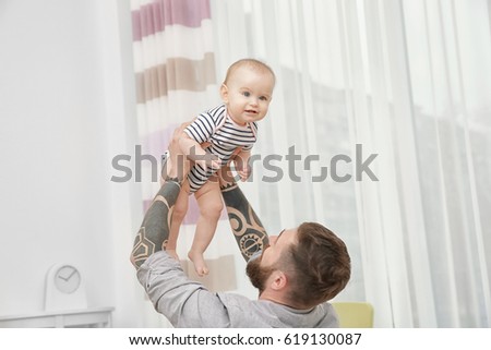 Handsome tattooed young man playing with cute little baby at home
