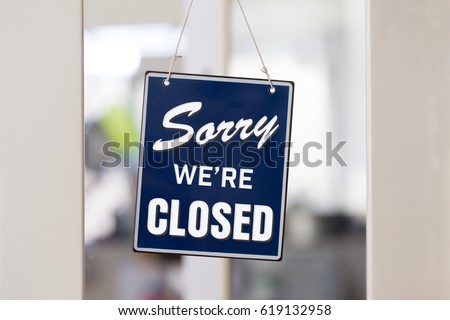 " Sorry we're closed " sign in blue and white, on shop glass door with white panels.