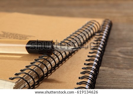 The old penholder with the pen lies on the notebooks sewn with metal springs on a wooden table. Retro stylized photo. Close-up