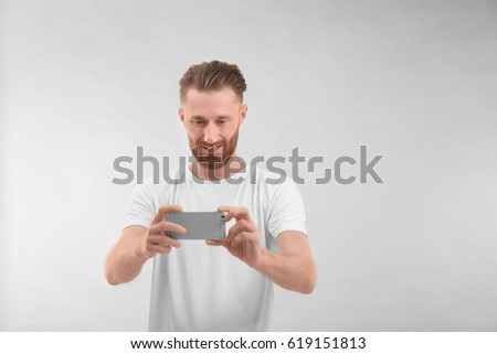Handsome man taking photo using mobile phone, on light background
