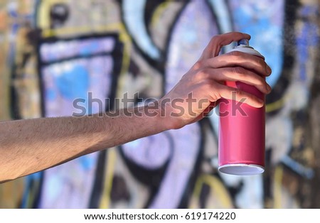 Photo of the hand of a street artist who draws a new color picture on a brick wall. One of the types of street art is the culture of youth graffiti. Decoration of walls of abandoned buildings