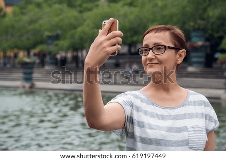 Women taking picture selfie. Nice portrait of a beautiful middle aged woman in her forties fifties holding phone and taking pictures outdoor in a summer day in the city.