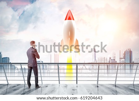 Rear view of a businessman standing on a balcony and looking at a red and white rocket taking off in a city. Toned image