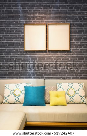 Colorful pillows and cushion on a modern style fabric sofa and white picture frames on a dark gray brick wall.