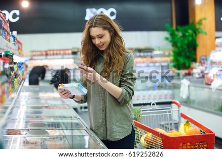 Cheerful brunette woman photographing product in supermarket