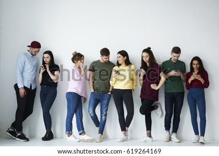 Full length portrait of group of diverse people use smartphones against copy space background with area for your advertising. Young friends in casual wear holding cellphones  using popular application Royalty-Free Stock Photo #619264169