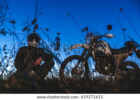 Active way of life, journey on a enduro motorcycle, a guy looks at the stars at night and the moon, unity with nature, the spirit of adventure, escape from the hustle and bustle of the city