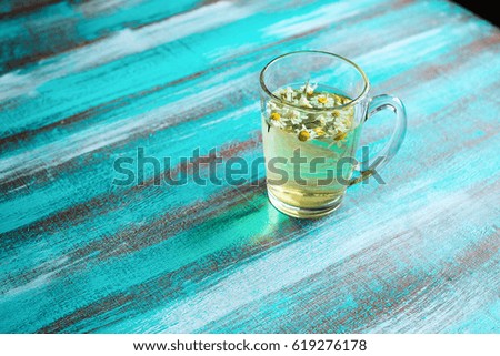 Chamomile tea in a clear glass cup on a turquoise background.