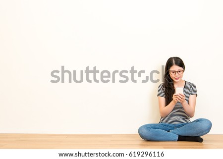 young female homeworker live video on the streaming with new mobile phone sitting on the wooden floor over empty area with white wall background.