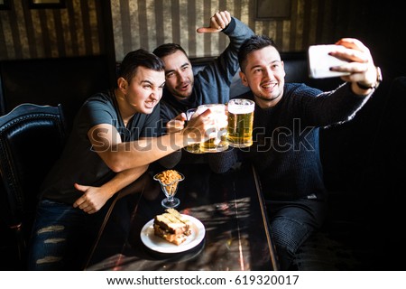 people, leisure, friendship, technology and party concept - happy male friends taking selfie and drinking beer at bar or pub