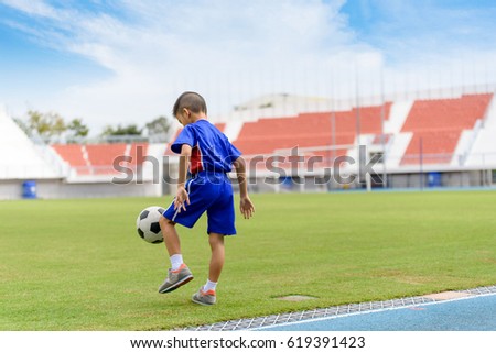 Young Asian Thai boy play on the grass football field in the stadium during summer